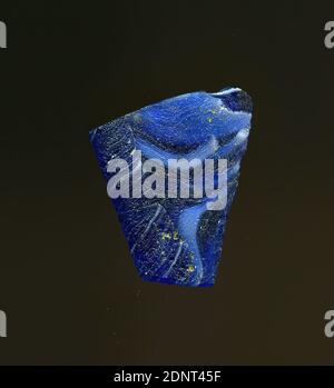 Fragment eines Gefäßes, Glas, gepresst, geschnitten, Gesamt: Höhe: 1.20 cm; Breite: 1.40 cm; Tiefe: 0.20 cm, Behälter, Lagerung, Küchenarbeit, frühkaiserliche Zeit, EINE leichte Krümmung des Glasfragments und der erhaltene Rand erlauben die Zuordnung zu einem Gefäß, möglicherweise einer Schüssel. Der blaue Boden ist mit mehreren weißen Streifen durchsetzt, von denen einige spiralförmig verlaufen. Für die Herstellung wurden verschiedenfarbige Gläser zu Rohren und Stäben geformt. Diese wurden zusammengedrückt und erhitzt, was zu einer langen Stange führte. Das in Scheiben geschnittene Glas hatte verschiedene amorphe oder florale Muster. Stockfoto