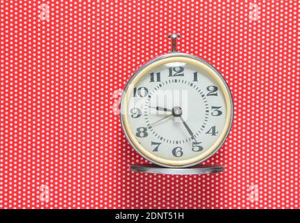 Retro-Wecker auf rotem Hintergrund in Polka-Punkt. Draufsicht Stockfoto