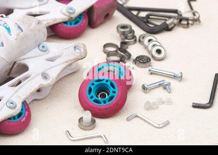 Austausch des Schlittschuhrollenlagers. Demontierte Rollschuhe, neue und verschlissene Lager, Achsen, Buchsen, Schrauben und Sechskantschlüssel. Stockfoto