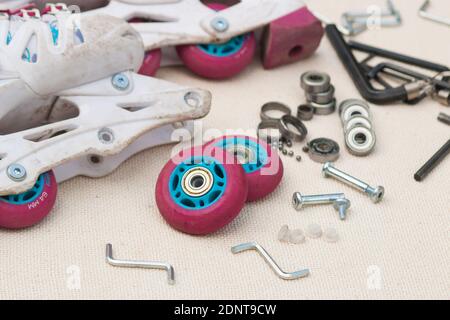 Austausch des Schlittschuhrollenlagers. Demontierte Rollschuhe, neue und verschlissene Lager, Achsen, Buchsen, Schrauben und Sechskantschlüssel. Stockfoto