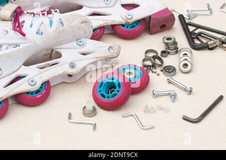 Austausch des Schlittschuhrollenlagers. Demontierte Rollschuhe, neue und verschlissene Lager, Achsen, Buchsen, Schrauben und Sechskantschlüssel. Stockfoto