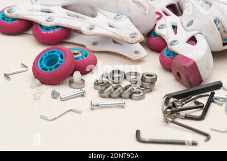 Austausch des Schlittschuhrollenlagers. Demontierte Rollschuhe, neue und verschlissene Lager, Achsen, Buchsen, Schrauben und Sechskantschlüssel. Stockfoto