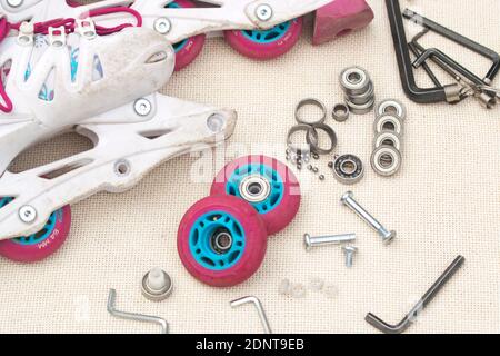Austausch des Schlittschuhrollenlagers. Demontierte Rollschuhe, neue und verschlissene Lager, Achsen, Buchsen, Schrauben und Sechskantschlüssel. Stockfoto