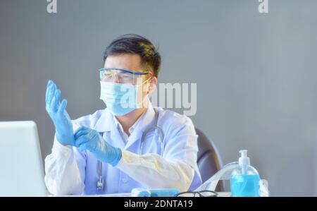 Porträt eines Arztes, der an seinem Schreibtisch sitzt und sich aufsetzt OP-Handschuhe Stockfoto
