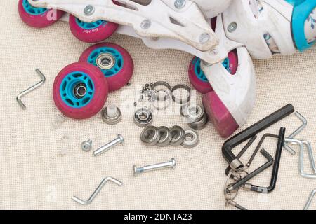 Austausch des Schlittschuhrollenlagers. Demontierte Rollschuhe, neue und verschlissene Lager, Achsen, Buchsen, Schrauben und Sechskantschlüssel. Stockfoto