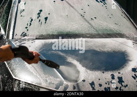 Autowäsche mit Hochdruckwasserstrahl. Wasser und Schaum fliegen unter Druck zur Karosserie. Nahaufnahme Stockfoto