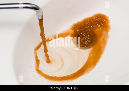 Schmutziges Wasser aus dem Wasserhahn. Rostiges Wasser fließt aus einem Wasserhahn in ein weißes Waschbecken Stockfoto