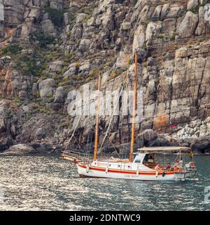Krim, Russland - 23. Februar 2017: Segelyacht und Boot segeln entlang der felsigen Küste des Schwarzen Meeres zwischen Klippen und Bergen. Naturlandschaft. Peo Stockfoto