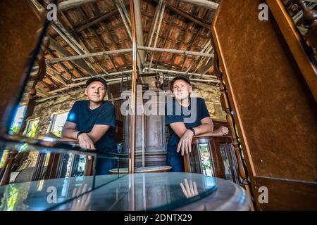 Spiegelung im Spiegel eines Mannes, der in die schaut Kamera in einem Lagerraum voller alter Holzmöbel Stockfoto