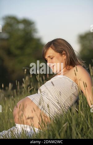 Eine schöne junge schwangere Frau mit ihrem ungeborenen Baby t Entspannen Sie sich draußen auf einem grünen Gras Stockfoto