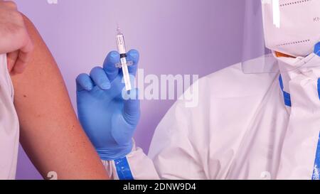 Impfkonzept für Coronaviren. Gettin Covid-19-Impfstoff. Der Patient erhält einen Covid-Impfstoff von einem Arzt, der einen Schutzanzug, eine Maske und ein Visier trägt. Stockfoto