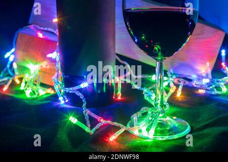 Weinglas und Flasche in glänzendem Girlande Bokeh auf schwarzem Hintergrund. Nahaufnahme Stockfoto