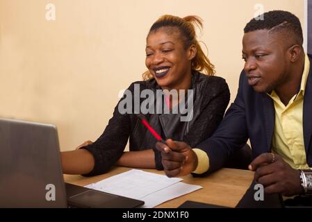 Junge Leute, die am Schreibtisch sitzen und dabei lächeln und auf den Laptop schauen. Stockfoto
