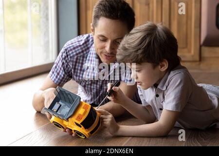 Fokussierter kleiner Sohn fix Spielzeugauto mit Hilfe von Papa Stockfoto
