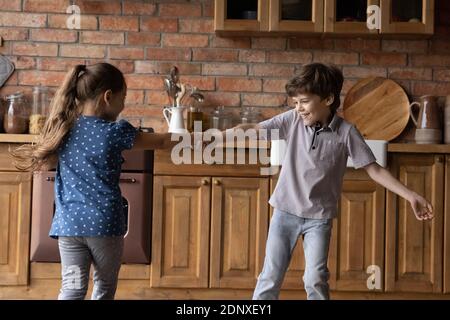 Fröhliche kleine Kinder Geschwister tanzen um die Küche herum und halten Hände Stockfoto