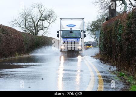 Moreton-on-Lugg, Herefordshire, UK - Friday 18th December 2020 - Vehicles drive through surface water flooding that has overspilled from the nearby River Lugg after another day of heavy rain across Herefordshire and Mid Wales. In Herefordshire both the River Wye and the River Lugg remain on Flood Alert and are exprected to rise. Photo Steven May / Alamy Live News Stock Photo