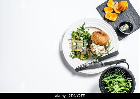 Burger mit Blauschimmelkäse, marmorierte Rind- und Zwiebelmarmelade, eine Beilage Salat mit Rucola und Orangen. Weißer Hintergrund. Draufsicht. Speicherplatz kopieren. Stockfoto