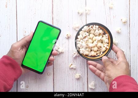 Mann Hand mit Smartphone und essen Popcorn Stockfoto