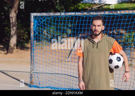 Schöner Hipster-Fußballspieler vor dem Tor eines Stadtplatzes mit dem Ball unter dem Arm, Konzept des gesunden Lebensstils und Stadtsport in der Stockfoto