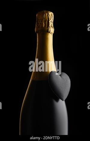 Valentinstagskonzept: Nahaufnahme einer Flasche Champagner mit schwarzem Herz vor schwarzem Hintergrund. Stockfoto