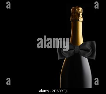 Nahaufnahme einer ungeöffneten Flasche Champagner auf schwarzem Hintergrund mit schwarzer Fliege. Ideal für Hochzeit, Jubiläum oder Neujahr Projekte, mit c Stockfoto