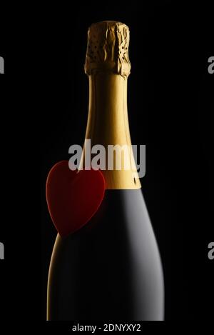 Valentinstagskonzept: Nahaufnahme einer Flasche Champagner mit rotem Herz vor schwarzem Hintergrund. Stockfoto