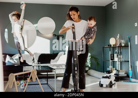 Frau trägt Kleinkind und Staubsaugerraum Stockfoto