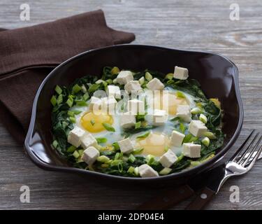 Grüne Shakshuka mit Spinat, Lauch und Feta in einer keramischen Bratpfanne auf einem Holztisch, selektiver Fokus. Köstliche gesunde Hausnahrung Stockfoto