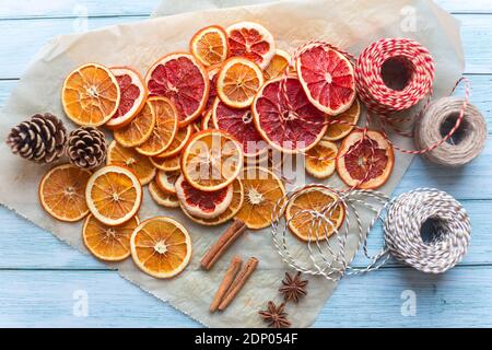 Zimt, Anis, getrocknete Orangen und Grapefruitscheiben, Fäden für diy-Projekte, Geschenkverpackung und schöne Öko-Weihnachtsdekorationen wie Kränze auf einem blauen Holztisch angeordnet Stockfoto