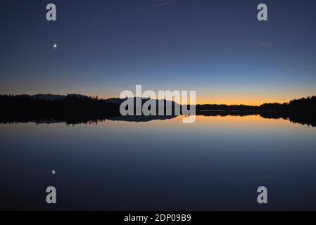 Wachende Mondsichel Spiegelung im Kirchsee in der Abenddämmerung, Bayern, Deutschland Stockfoto