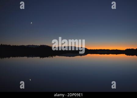 Wachende Mondsichel Spiegelung im Kirchsee in der Abenddämmerung, Bayern, Deutschland Stockfoto