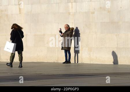 London, England, Großbritannien. Mann filmt auf seinem Handy am Trafalgar Square, Dezember 2020 Stockfoto