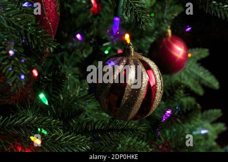 Nahaufnahme von roten und goldenen glitzernden weihnachtsbaumschmuck hing Von einem weihnachtsbaum mit Baumleuchten und Bokeh-Effekt Leuchtet Stockfoto