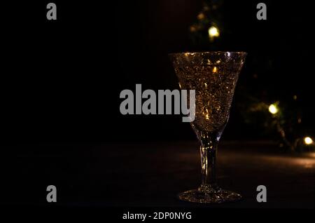 Glas mit Weißwein mit Girlande Lichter auf dem Hintergrund. Dunkles Bild. Goldenes Getränk im Glas. Schöne Lichter im Glas reflektiert. Stockfoto
