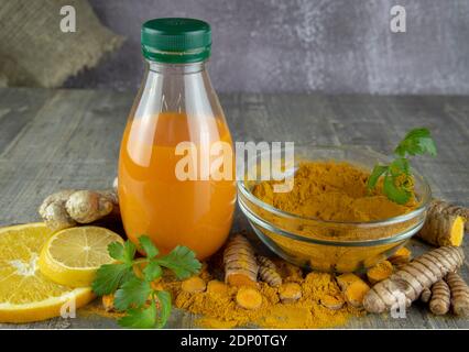 Kurkuma-Saft in einer Flasche, Zitrone, Orange und Kurkuma-Pulver auf Holzgrund. Stockfoto