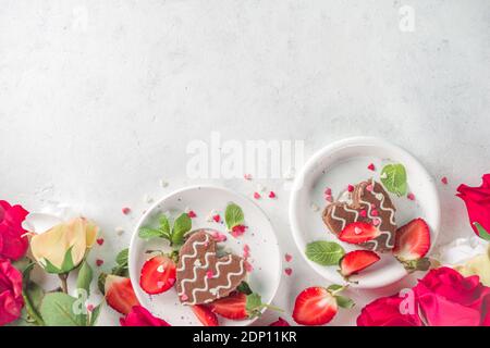 Dessert am Valentinstag. Herzförmige Biskuit Schokolade Mini-Kuchen mit Erdbeere und Minze. Draufsicht auf weißem Hintergrund mit Rosen Blumen kopieren Raum Stockfoto