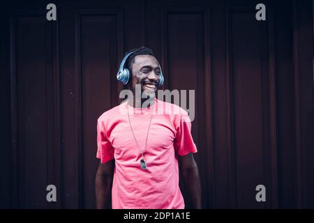 Lachender Mann mit pinkem T-Shirt, der mit Kopfhörern Musik hört Stockfoto