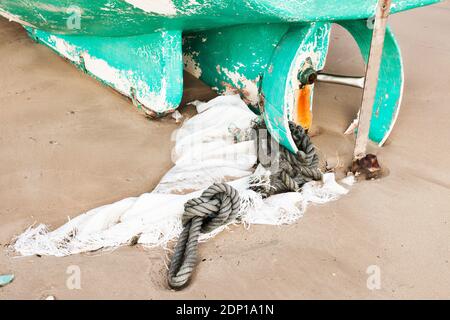 Teil eines grünen Bootes auf dem Sand mit sitzen Ein braunes Seil und ein weißes Netz am Propeller Stockfoto