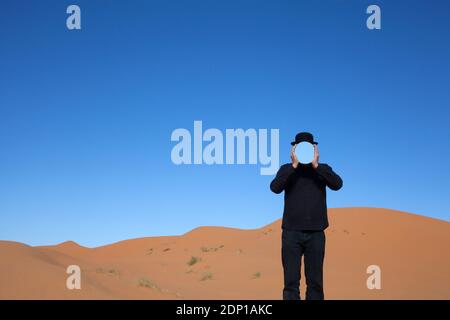 Marokko, Merzouga, Erg Chebbi, Mann, eine Melone holding Spiegel vor sein Gesicht in der Wüste Düne Stockfoto