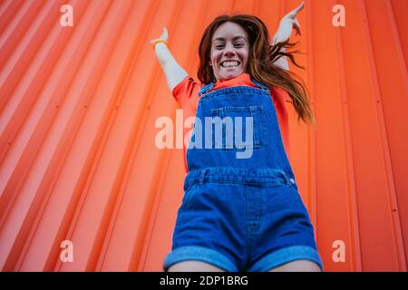 Junge Frau, die gegen die orangefarbene Wand springt Stockfoto