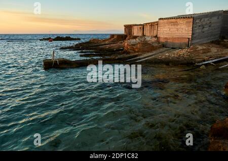 Traditionelle Bootshäuser, die Escars genannt werden, bei Sonnenuntergang in der Nähe der Meereslagune Estany des Peix im Naturpark Ses Salines (Formentera, Mittelmeer, Spanien) Stockfoto