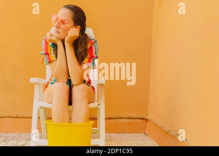 Portrait der Frau entspannen auf Kunststoff-Stuhl Kühlung ihre Beine Im Eimer mit Wasser Stockfoto