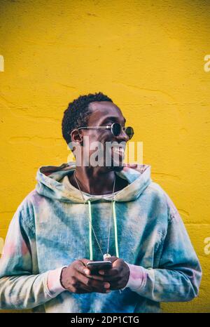 Portrait von lächelnden jungen Mann mit Smartphone vor der gelben wand Stockfoto