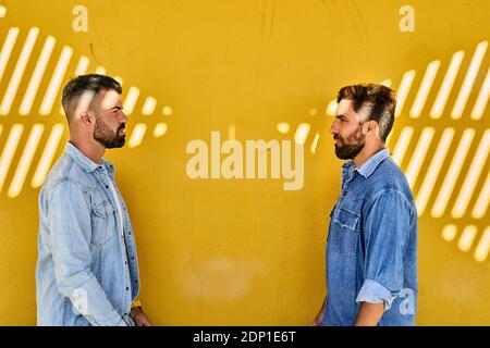 Gay couple looking at each other while standing against yellow wall Stockfoto