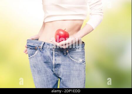 Junge schlanke Frau in überdimensionalen Jeans mit einem Apfel Grüner Hintergrund Stockfoto