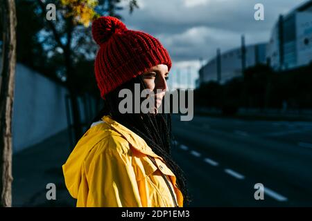 Nachdenkliche Frau in Strickmütze, die während des Sonnenuntergangs auf der Straße steht Stockfoto