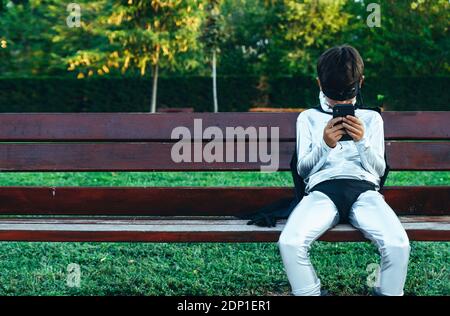 Portrait der Junge getarnt als mit Handy auf parkbank Superhelden Stockfoto