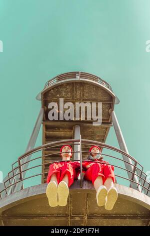 Junges Paar mit roten Overalls und Hüten, die nebeneinander sitzen Seite auf Plattform mit Blick auf die Entfernung Stockfoto