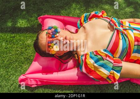 Portrait der Frau trägt eine Brille mit bunten Pom Poms Abdeckung Ihre Augen entspannen sich auf dem rosa Luftbett Stockfoto