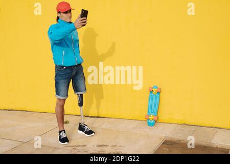 Mann mit Mütze, der Selfie nimmt, während er an der gelben Wand steht Stockfoto